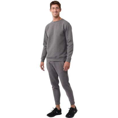 A man is wearing the Men's StretchTech Crewneck sweatshirt from Cozy Earth, paired with matching sweatpants. He stands against a plain white background with short brown hair, looking forward with a neutral expression. |Color:Coal Heather