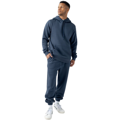 A person with curly hair is wearing a Cozy Earth Men's CityScape Hoodie in dark green and standing against a plain white background, with their hands together. |Color:Spruce