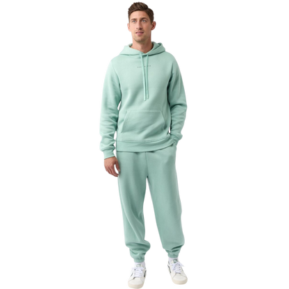 A person with curly hair is wearing a Cozy Earth Men's CityScape Hoodie in dark green and standing against a plain white background, with their hands together. |Color:Spruce