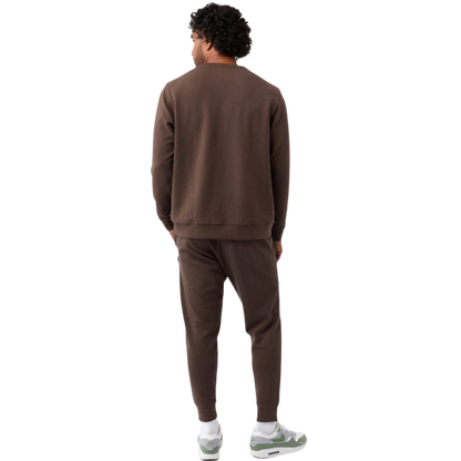 A man is wearing the Men's StretchTech Crewneck sweatshirt from Cozy Earth, paired with matching sweatpants. He stands against a plain white background with short brown hair, looking forward with a neutral expression. |Color:Coal Heather