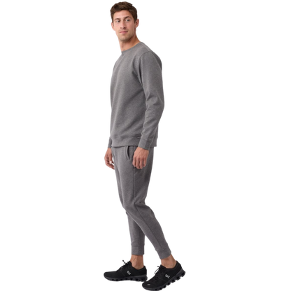 A man is wearing the Men's StretchTech Crewneck sweatshirt from Cozy Earth, paired with matching sweatpants. He stands against a plain white background with short brown hair, looking forward with a neutral expression. |Color:Coal Heather