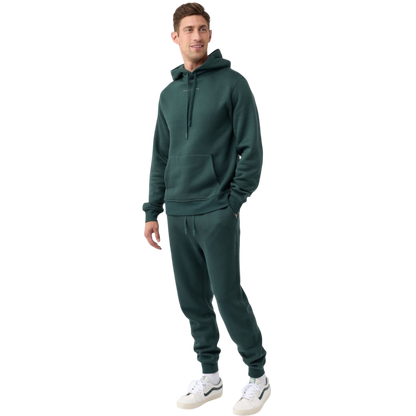 A person with curly hair is wearing a Cozy Earth Men's CityScape Hoodie in dark green and standing against a plain white background, with their hands together. |Color:Spruce