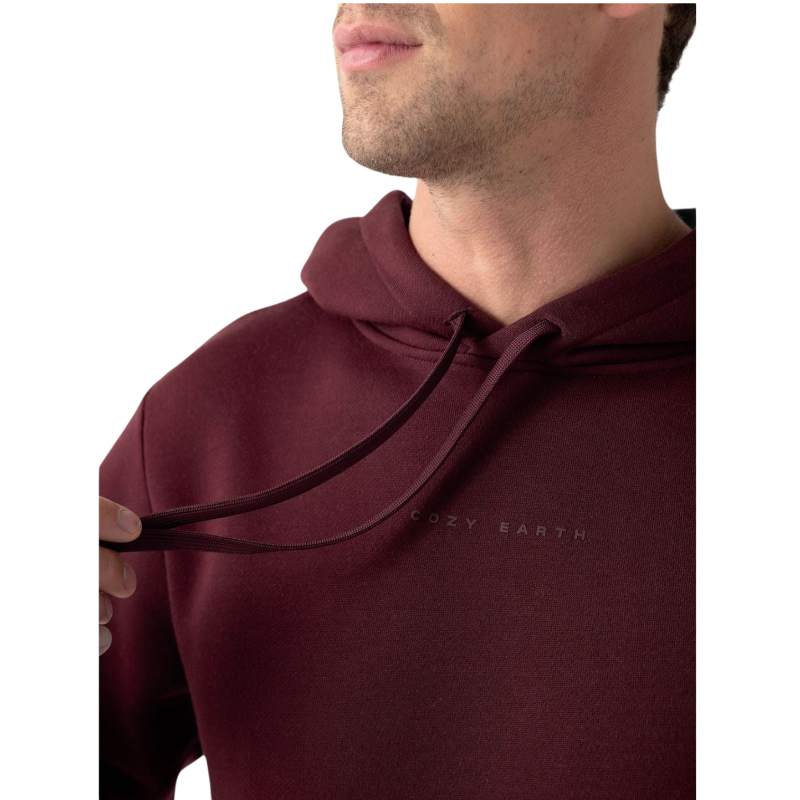 A person with curly hair is wearing a Cozy Earth Men's CityScape Hoodie in dark green and standing against a plain white background, with their hands together. |Color:Spruce