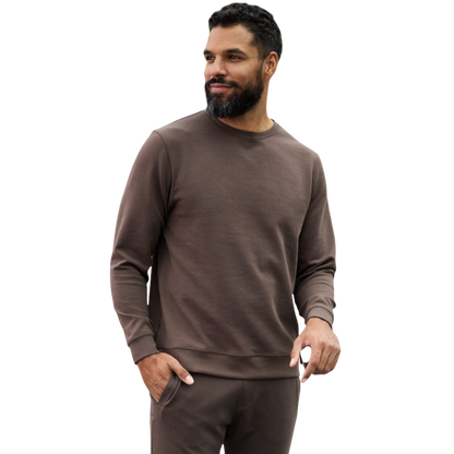 A man is wearing the Men's StretchTech Crewneck sweatshirt from Cozy Earth, paired with matching sweatpants. He stands against a plain white background with short brown hair, looking forward with a neutral expression. |Color:Coal Heather