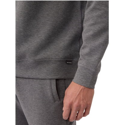 A man is wearing the Men's StretchTech Crewneck sweatshirt from Cozy Earth, paired with matching sweatpants. He stands against a plain white background with short brown hair, looking forward with a neutral expression. |Color:Coal Heather