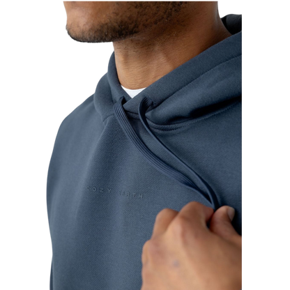 A person with curly hair is wearing a Cozy Earth Men's CityScape Hoodie in dark green and standing against a plain white background, with their hands together. |Color:Spruce