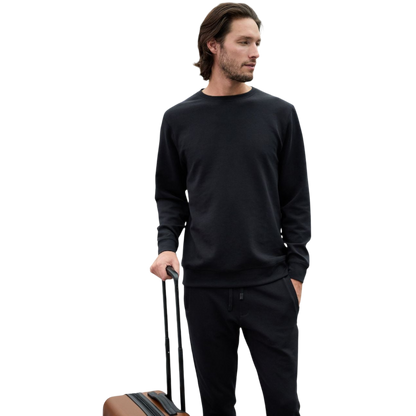 A man is wearing the Men's StretchTech Crewneck sweatshirt from Cozy Earth, paired with matching sweatpants. He stands against a plain white background with short brown hair, looking forward with a neutral expression. |Color:Coal Heather