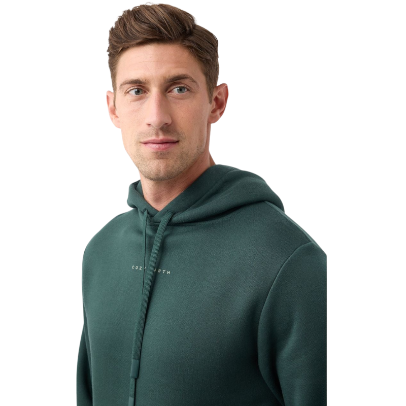 A person with curly hair is wearing a Cozy Earth Men's CityScape Hoodie in dark green and standing against a plain white background, with their hands together. |Color:Spruce
