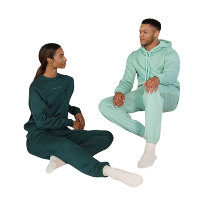 A person with curly hair is wearing a Cozy Earth Men's CityScape Hoodie in dark green and standing against a plain white background, with their hands together. |Color:Spruce