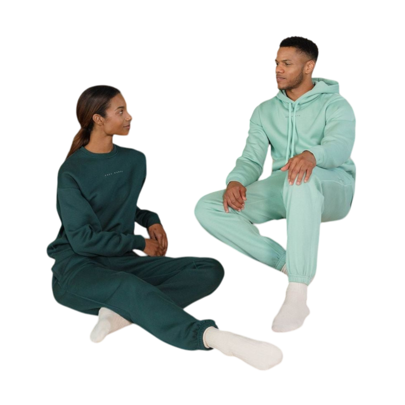 A person with curly hair is wearing a Cozy Earth Men's CityScape Hoodie in dark green and standing against a plain white background, with their hands together. |Color:Spruce