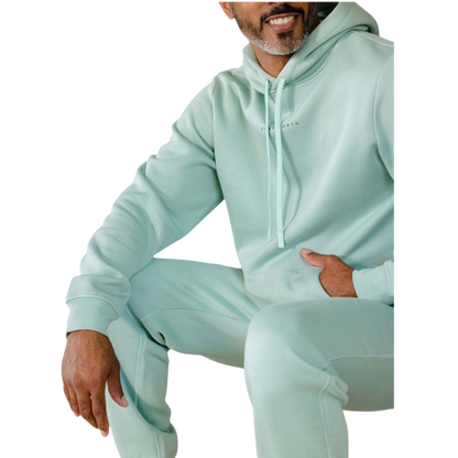 A person with curly hair is wearing a Cozy Earth Men's CityScape Hoodie in dark green and standing against a plain white background, with their hands together. |Color:Spruce