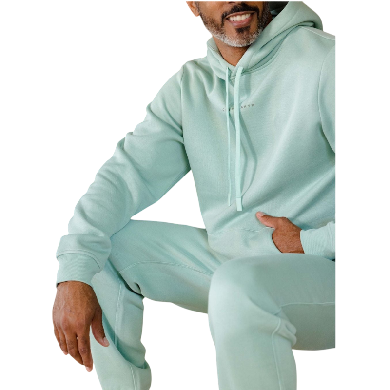 A person with curly hair is wearing a Cozy Earth Men's CityScape Hoodie in dark green and standing against a plain white background, with their hands together. |Color:Spruce