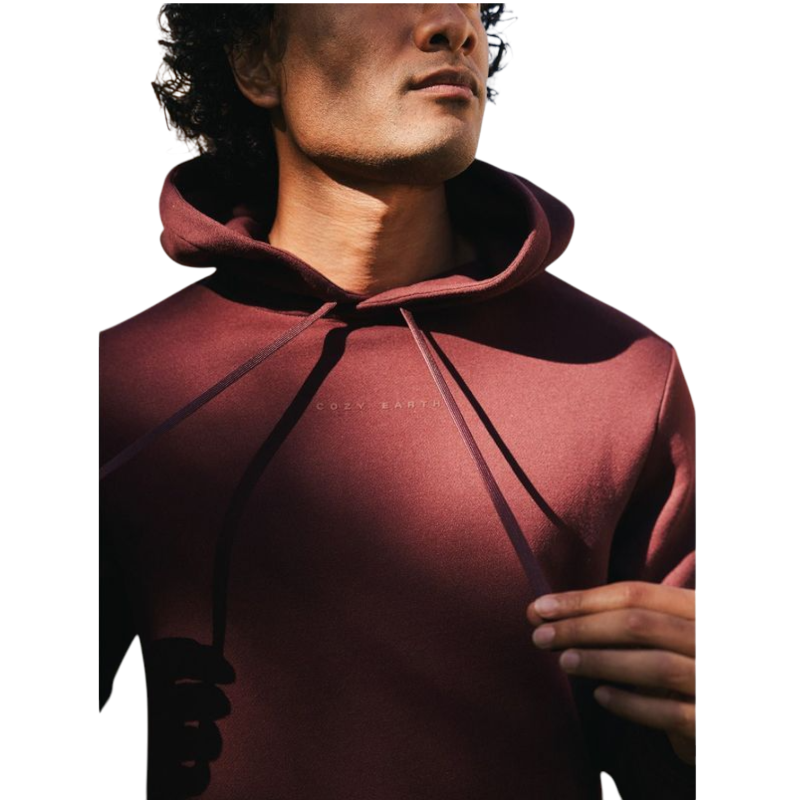 A person with curly hair is wearing a Cozy Earth Men's CityScape Hoodie in dark green and standing against a plain white background, with their hands together. |Color:Spruce