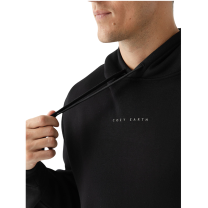 A person with curly hair is wearing a Cozy Earth Men's CityScape Hoodie in dark green and standing against a plain white background, with their hands together. |Color:Spruce