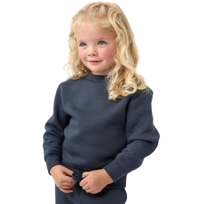 A young boy with blond hair is wearing the Cozy Earth Kid's CityScape Crewneck sweatshirt along with matching pants. He is standing, smiling, and looking slightly to the side against a plain white background. |Color:Eclipse