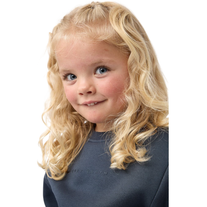 A young boy with blond hair is wearing the Cozy Earth Kid's CityScape Crewneck sweatshirt along with matching pants. He is standing, smiling, and looking slightly to the side against a plain white background. |Color:Eclipse