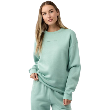 A young girl with long brown hair smiles at the camera, wearing the light green Kid's CityScape Crewneck from Cozy Earth along with matching pants. The background is plain white. |Color:Wintergreen