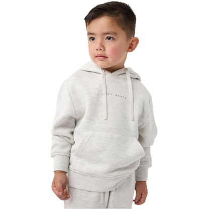 A young boy with short brown hair stands against a white background, wearing the Cozy Earth Kid's CityScape Hoodie, a light gray piece with subtle text on it, paired with matching sweatpants. He gazes to the side with a thoughtful expression. |Color:Heather Grey