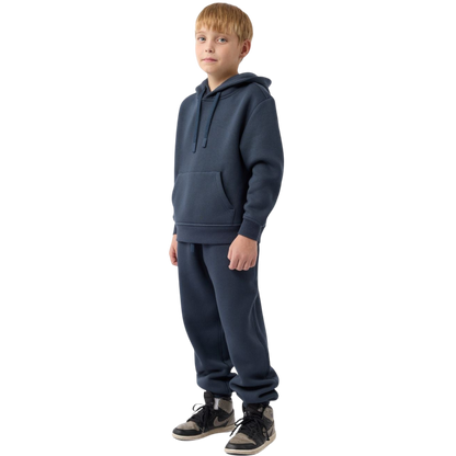 A young child with long blonde hair smiles while wearing a navy blue Kid's CityScape Hoodie by Cozy Earth and matching pants. She has two hair ties, one pink and one blue. The background is plain white. |Color:Eclipse