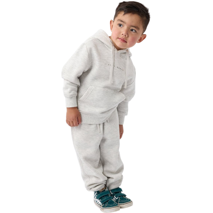 A young child with long blonde hair smiles while wearing a navy blue Kid's CityScape Hoodie by Cozy Earth and matching pants. She has two hair ties, one pink and one blue. The background is plain white. |Color:Eclipse