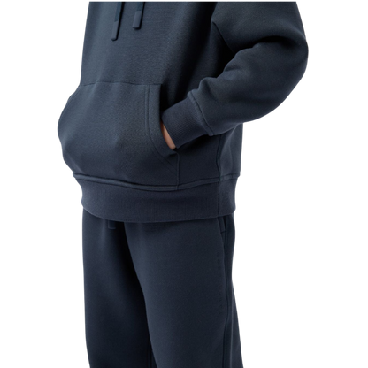 A young child with long blonde hair smiles while wearing a navy blue Kid's CityScape Hoodie by Cozy Earth and matching pants. She has two hair ties, one pink and one blue. The background is plain white. |Color:Eclipse