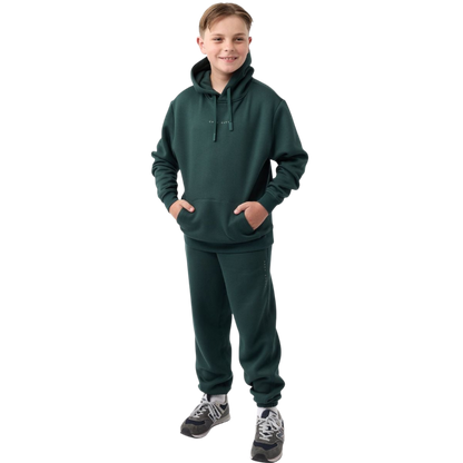 A young child with long blonde hair smiles while wearing a navy blue Kid's CityScape Hoodie by Cozy Earth and matching pants. She has two hair ties, one pink and one blue. The background is plain white. |Color:Eclipse