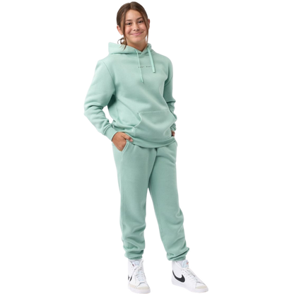 A young child with long blonde hair smiles while wearing a navy blue Kid's CityScape Hoodie by Cozy Earth and matching pants. She has two hair ties, one pink and one blue. The background is plain white. |Color:Eclipse