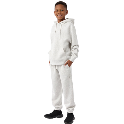 A young child with long blonde hair smiles while wearing a navy blue Kid's CityScape Hoodie by Cozy Earth and matching pants. She has two hair ties, one pink and one blue. The background is plain white. |Color:Eclipse