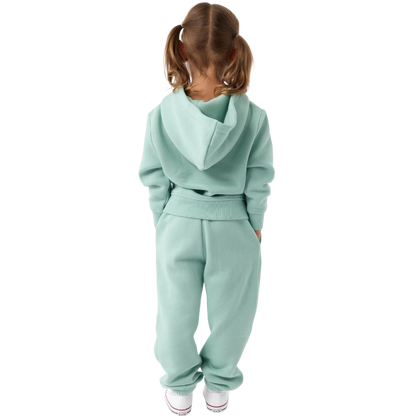 A young child with long blonde hair smiles while wearing a navy blue Kid's CityScape Hoodie by Cozy Earth and matching pants. She has two hair ties, one pink and one blue. The background is plain white. |Color:Eclipse