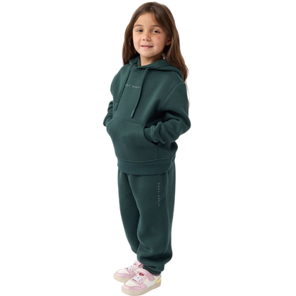 A young child with long blonde hair smiles while wearing a navy blue Kid's CityScape Hoodie by Cozy Earth and matching pants. She has two hair ties, one pink and one blue. The background is plain white. |Color:Eclipse