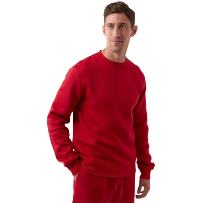A person wearing a matching red Men's CityScape Crewneck and pants from Cozy Earth stands against a plain white background. They have short hair, are looking to the side with a slight smile, and have one hand in their pocket. |Color:Crimson