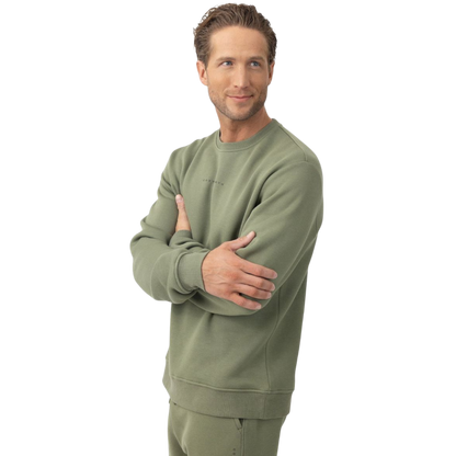 A man with short brown hair is wearing a dark green Men's CityScape Crewneck from Cozy Earth, featuring the words "COLD EARTH" printed on it. He is gazing slightly to the side against a plain white background. |Color:Spruce