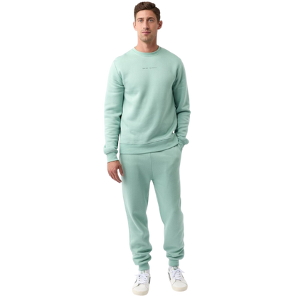 A man with short brown hair is wearing a dark green Men's CityScape Crewneck from Cozy Earth, featuring the words "COLD EARTH" printed on it. He is gazing slightly to the side against a plain white background. |Color:Spruce