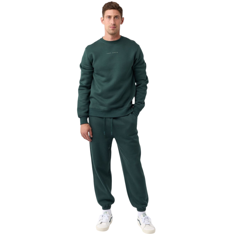 A man with short brown hair is wearing a dark green Men's CityScape Crewneck from Cozy Earth, featuring the words "COLD EARTH" printed on it. He is gazing slightly to the side against a plain white background. |Color:Spruce