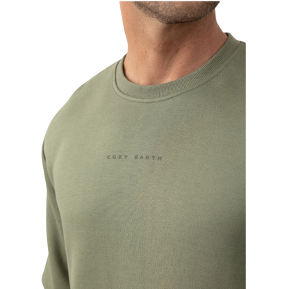A man with short brown hair is wearing a dark green Men's CityScape Crewneck from Cozy Earth, featuring the words "COLD EARTH" printed on it. He is gazing slightly to the side against a plain white background. |Color:Spruce