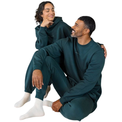 A man with short brown hair is wearing a dark green Men's CityScape Crewneck from Cozy Earth, featuring the words "COLD EARTH" printed on it. He is gazing slightly to the side against a plain white background. |Color:Spruce