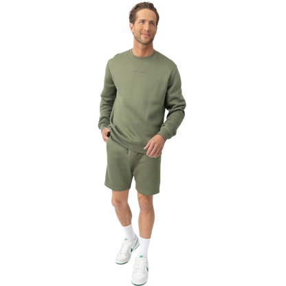 A man with short brown hair is wearing a dark green Men's CityScape Crewneck from Cozy Earth, featuring the words "COLD EARTH" printed on it. He is gazing slightly to the side against a plain white background. |Color:Spruce