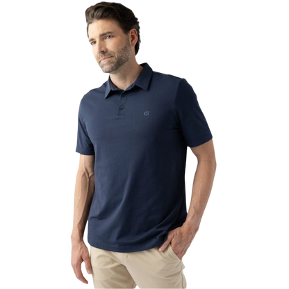 A man with a beard is wearing Cozy Earth's Men's Everyday Polo in dark navy and light beige pants. He is standing against a plain white background with one hand in his pocket, looking slightly to his left. |Color:Eclipse