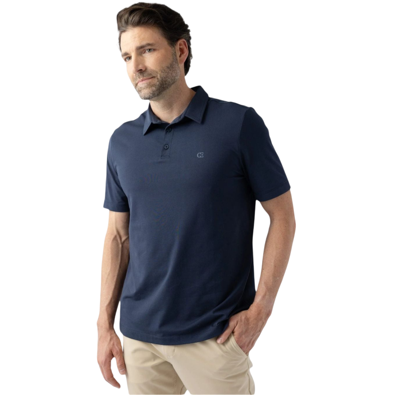 A man with a beard is wearing Cozy Earth's Men's Everyday Polo in dark navy and light beige pants. He is standing against a plain white background with one hand in his pocket, looking slightly to his left. |Color:Eclipse