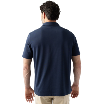 A person with short, light brown hair is wearing the Men's Everyday Polo by Cozy Earth in a light gray shade, paired with light beige pants. They are standing and slightly looking over their left shoulder with a neutral expression against a plain white background. |Color:Stone
