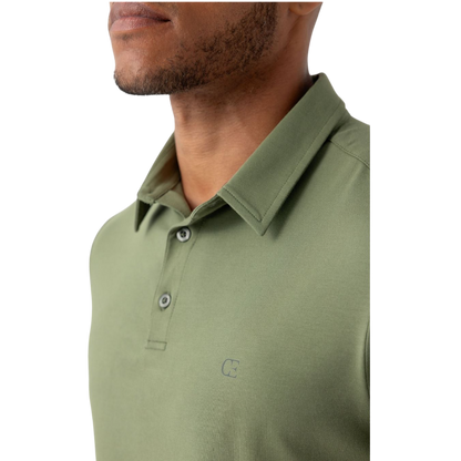 A person with short, light brown hair is wearing the Men's Everyday Polo by Cozy Earth in a light gray shade, paired with light beige pants. They are standing and slightly looking over their left shoulder with a neutral expression against a plain white background. |Color:Stone