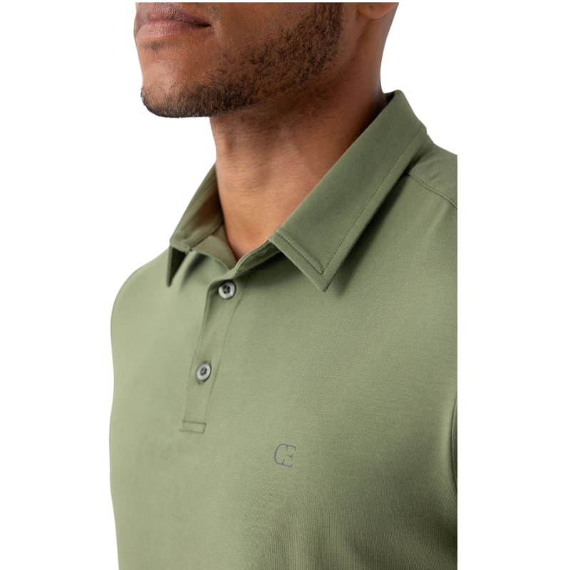 A person with short, light brown hair is wearing the Men's Everyday Polo by Cozy Earth in a light gray shade, paired with light beige pants. They are standing and slightly looking over their left shoulder with a neutral expression against a plain white background. |Color:Stone