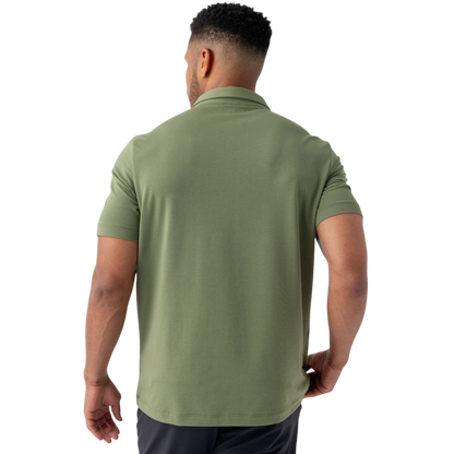 A person with short, light brown hair is wearing the Men's Everyday Polo by Cozy Earth in a light gray shade, paired with light beige pants. They are standing and slightly looking over their left shoulder with a neutral expression against a plain white background. |Color:Stone