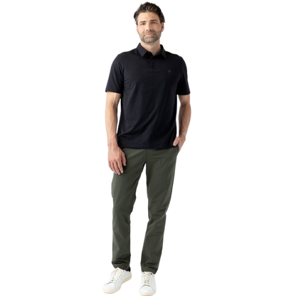 A person with short, light brown hair is wearing the Men's Everyday Polo by Cozy Earth in a light gray shade, paired with light beige pants. They are standing and slightly looking over their left shoulder with a neutral expression against a plain white background. |Color:Stone