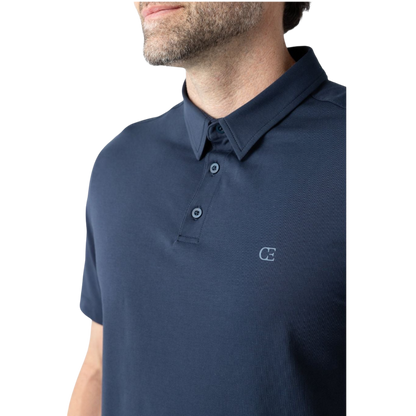 A person with short, light brown hair is wearing the Men's Everyday Polo by Cozy Earth in a light gray shade, paired with light beige pants. They are standing and slightly looking over their left shoulder with a neutral expression against a plain white background. |Color:Stone