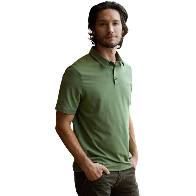 A person with short, light brown hair is wearing the Men's Everyday Polo by Cozy Earth in a light gray shade, paired with light beige pants. They are standing and slightly looking over their left shoulder with a neutral expression against a plain white background. |Color:Stone