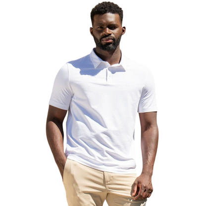 A person with short, light brown hair is wearing the Men's Everyday Polo by Cozy Earth in a light gray shade, paired with light beige pants. They are standing and slightly looking over their left shoulder with a neutral expression against a plain white background. |Color:Stone