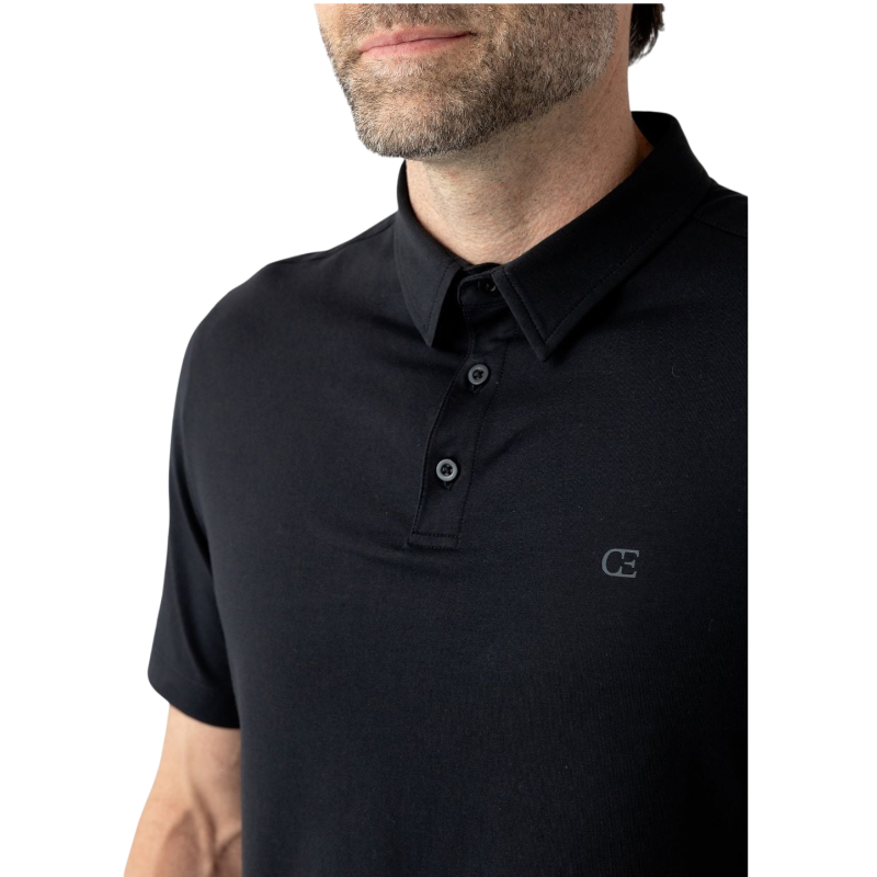 A person with short, light brown hair is wearing the Men's Everyday Polo by Cozy Earth in a light gray shade, paired with light beige pants. They are standing and slightly looking over their left shoulder with a neutral expression against a plain white background. |Color:Stone