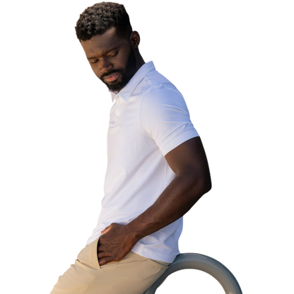 A person with short, light brown hair is wearing the Men's Everyday Polo by Cozy Earth in a light gray shade, paired with light beige pants. They are standing and slightly looking over their left shoulder with a neutral expression against a plain white background. |Color:Stone