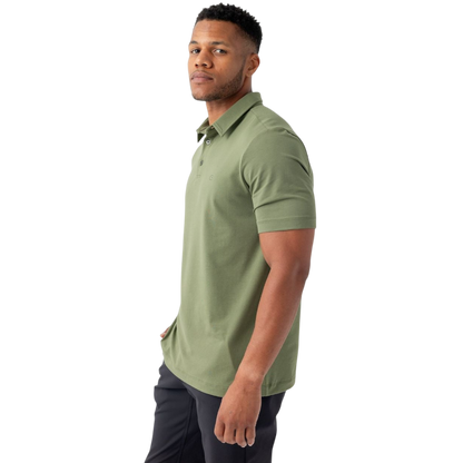 A person with short, light brown hair is wearing the Men's Everyday Polo by Cozy Earth in a light gray shade, paired with light beige pants. They are standing and slightly looking over their left shoulder with a neutral expression against a plain white background. |Color:Stone
